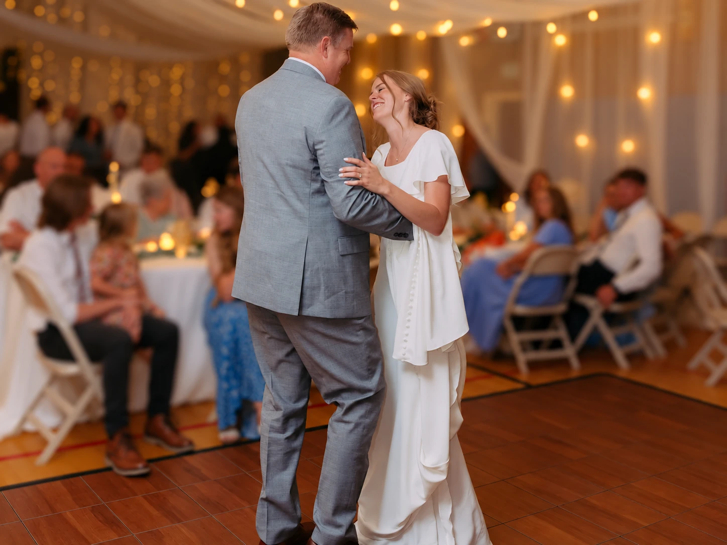 Family dancing on a dark maple dance floor, with background guests softly defocused
